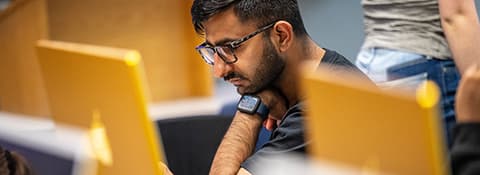 A man with glasses focused on his work in a computer lab