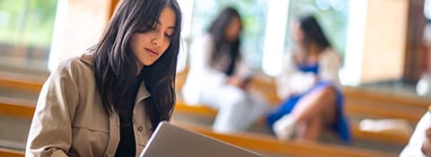 A student looks down at her laptop, sitting in an indoor study space