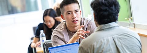 Two students sitting and talking face to face, with a laptop open