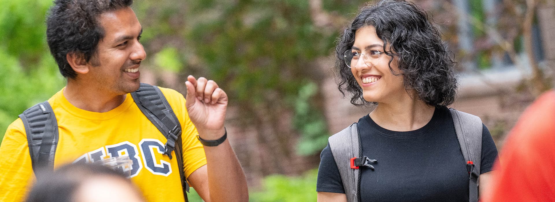 Two students smiling and looking at each other as they walk together outside on campus