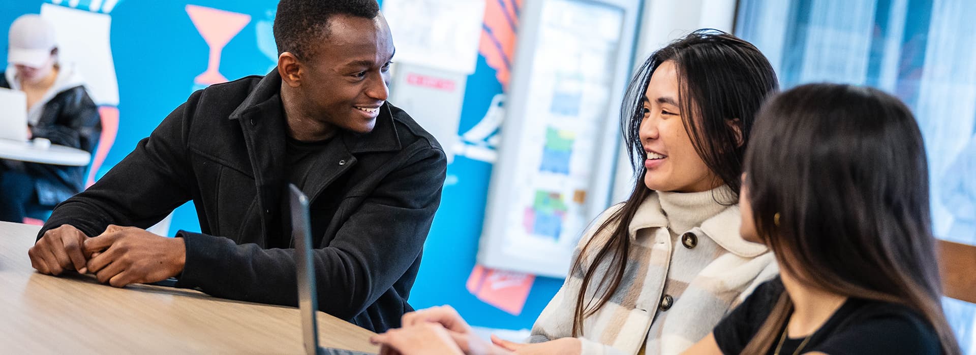 Three students sitting at a table in a study space, smiling